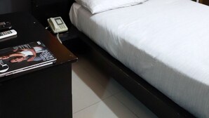 Una habitación de hotel con cama, una mesita de noche, un escritorio y una revista, y una pared con tres cuadros.