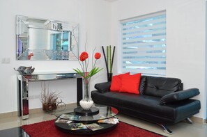 A modern living room with a black leather sofa, a red cushion, a glass coffee table, and a mirror above it. - Hotel Merey (Santo Domingo)