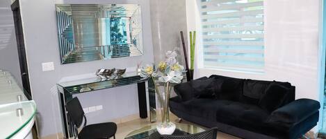 A modern living room with a glass dining table, black chairs, a black sofa, a decorative vase, and a large mirror on the wall.