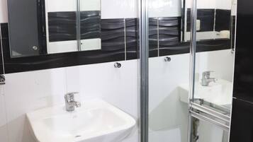Une salle de bain avec un lavabo blanc, un miroir et une cabine de douche en verre.