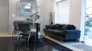 Una sala moderna con un sofá negro, una mesa de centro de vidrio y un jarrón decorativo.