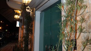 Entrada de un edificio con una puerta verde, luces decorativas en la pared y plantas en macetas.