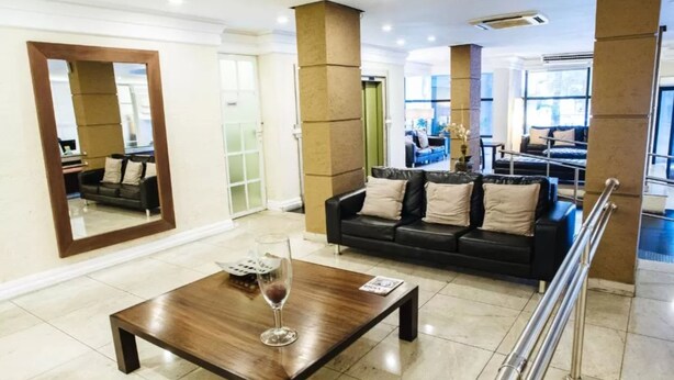 A modern living room with a wooden coffee table, a black leather sofa, and a large mirror. - Diamond Hotel (Rio de Janeiro)