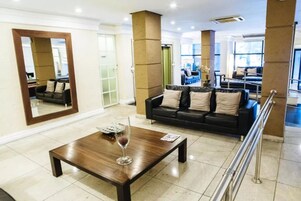 A modern living room with a wooden coffee table, a black leather sofa, and a large mirror.