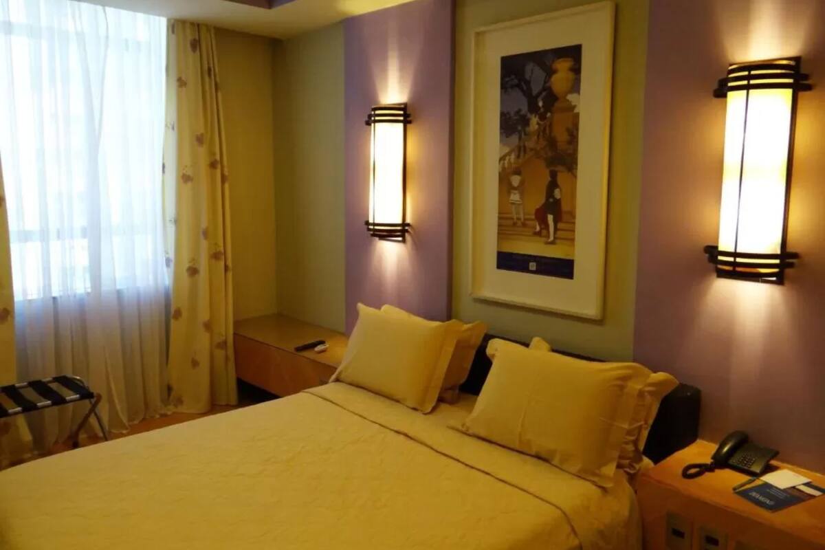 A hotel room with a bed, two bedside tables, a nightstand, a lamp, and a framed picture on the wall.