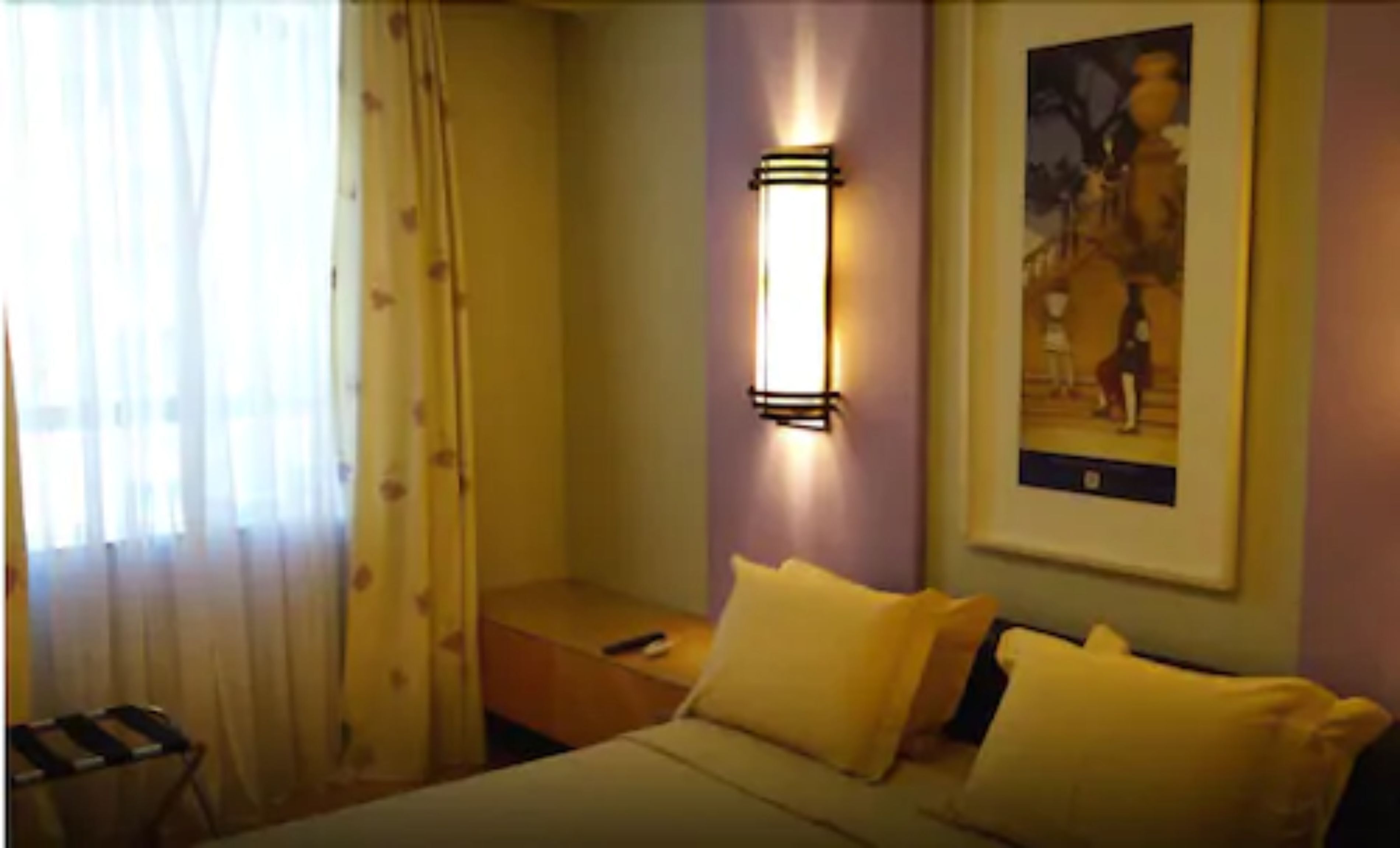 A hotel room with a bed, a nightstand, a lamp, and a painting on the wall.