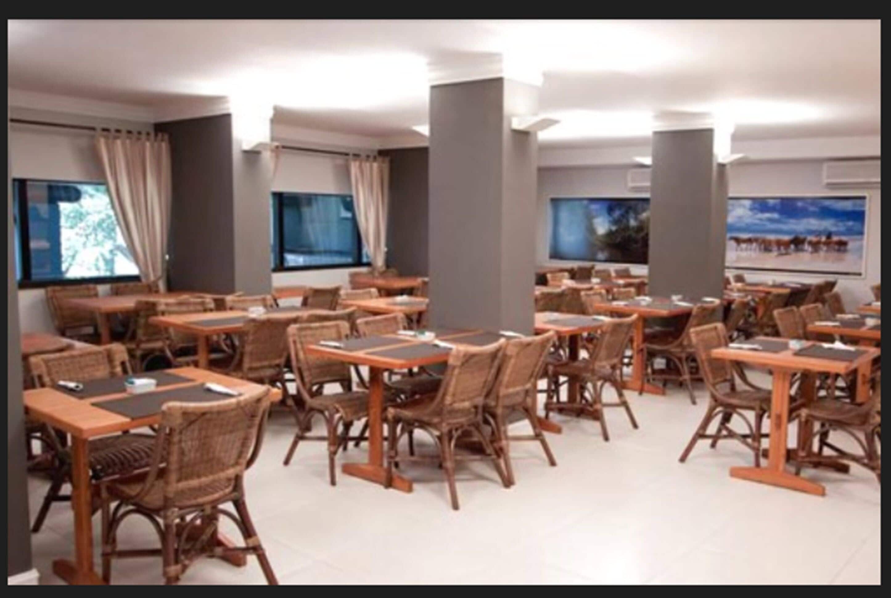 A spacious dining area with multiple tables and chairs, large windows, and a modern interior design.