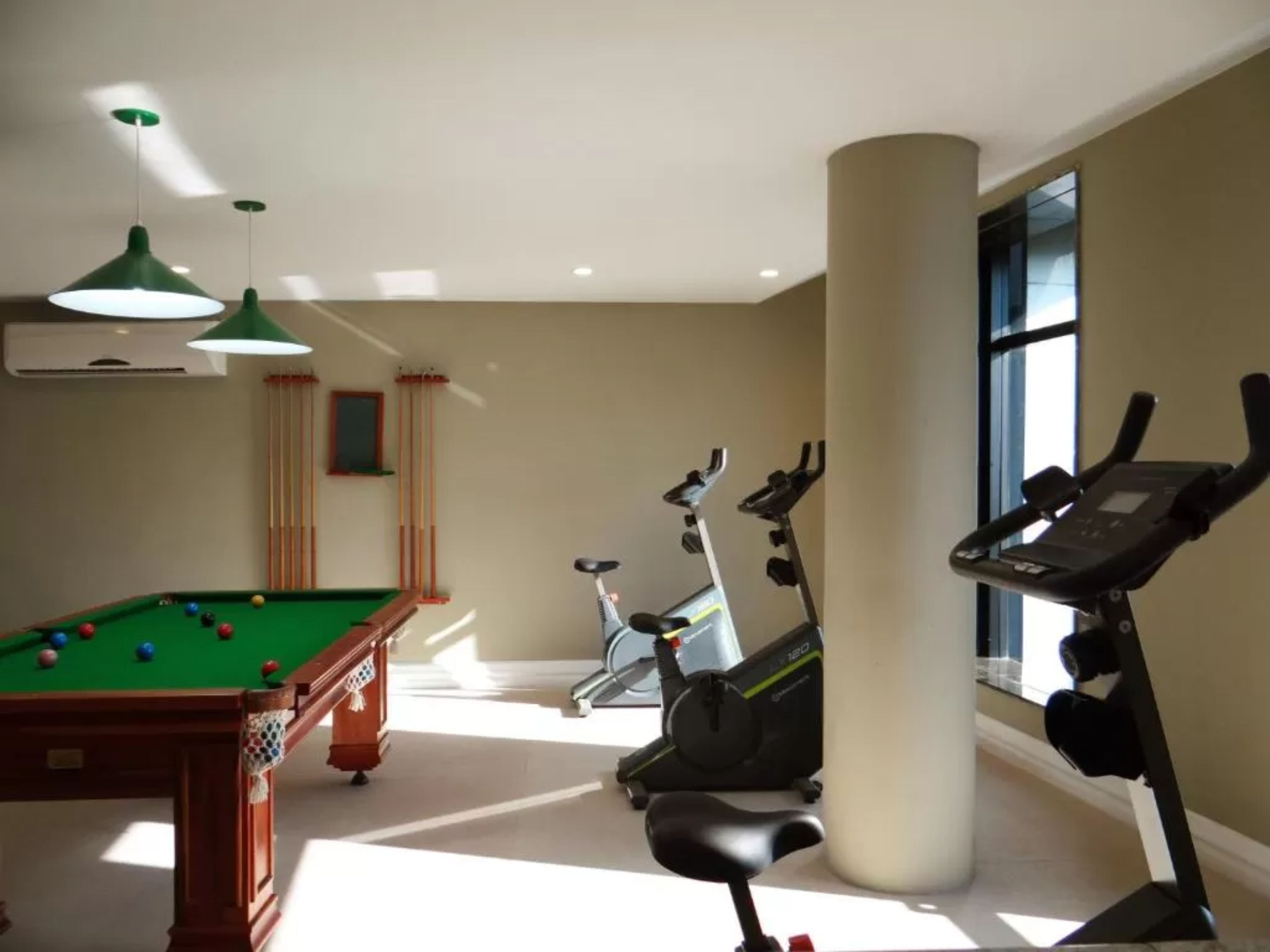 Quarto com mesa de bilhar, duas bicicletas ergométricas e uma janela grande.