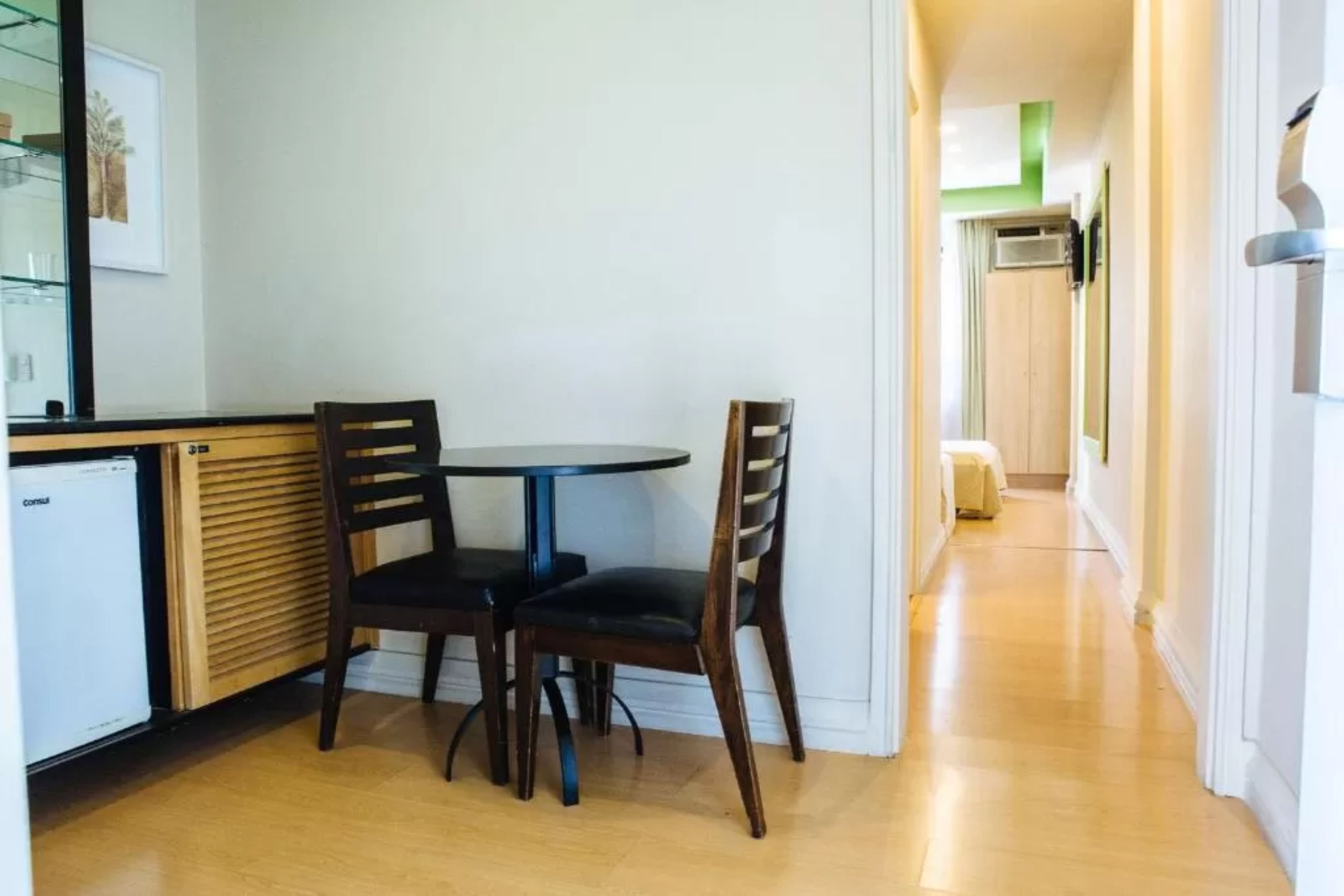 A compact kitchen with a round table and two chairs, a refrigerator, and a wooden cabinet.