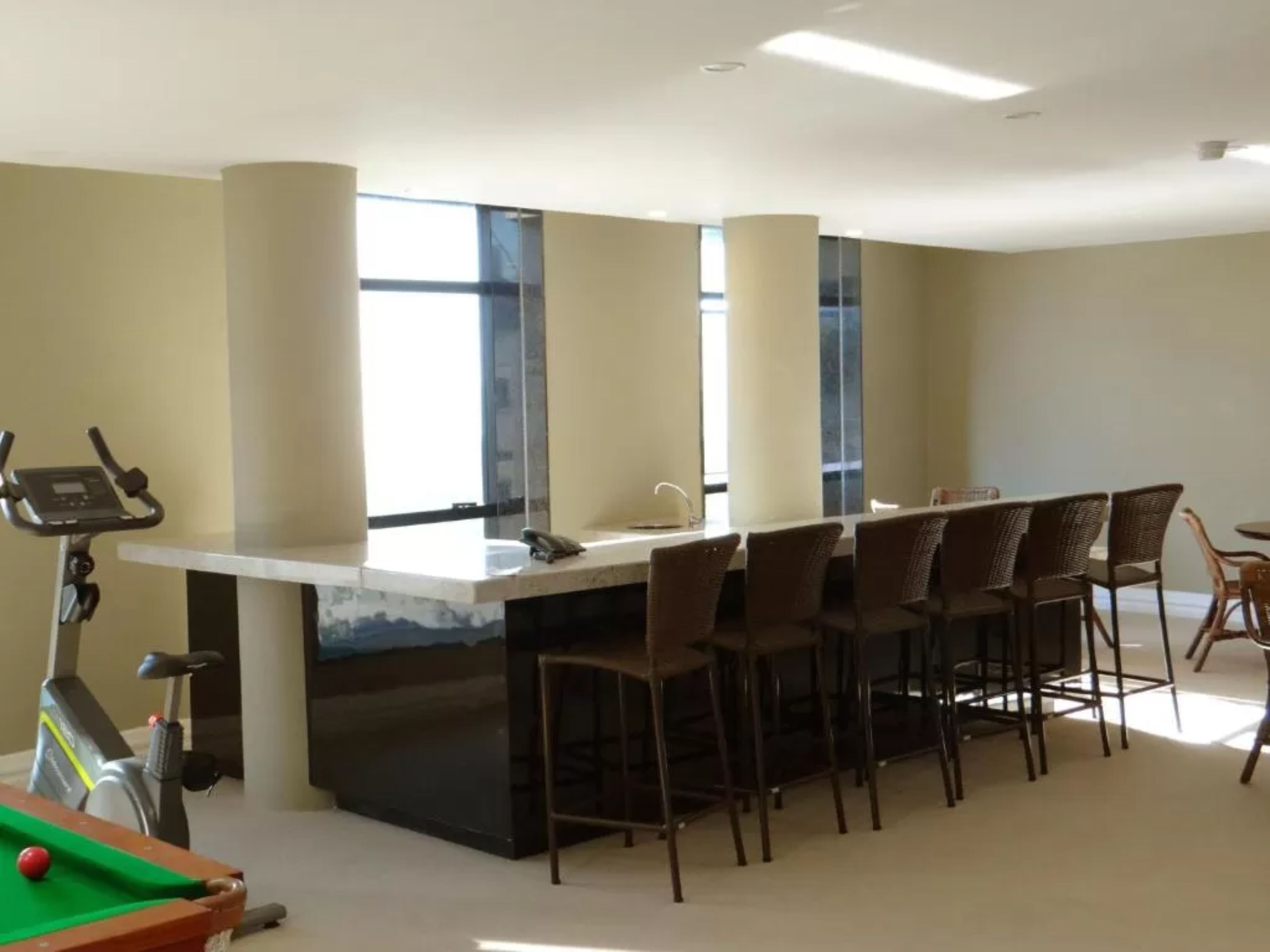 A room with a pool table, exercise bike, and a bar area with chairs.