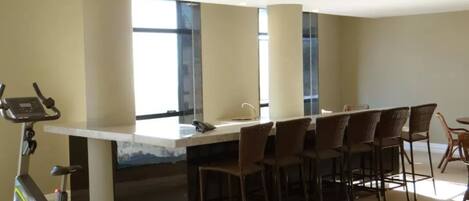 A room with a pool table, exercise bike, and a bar area with chairs.