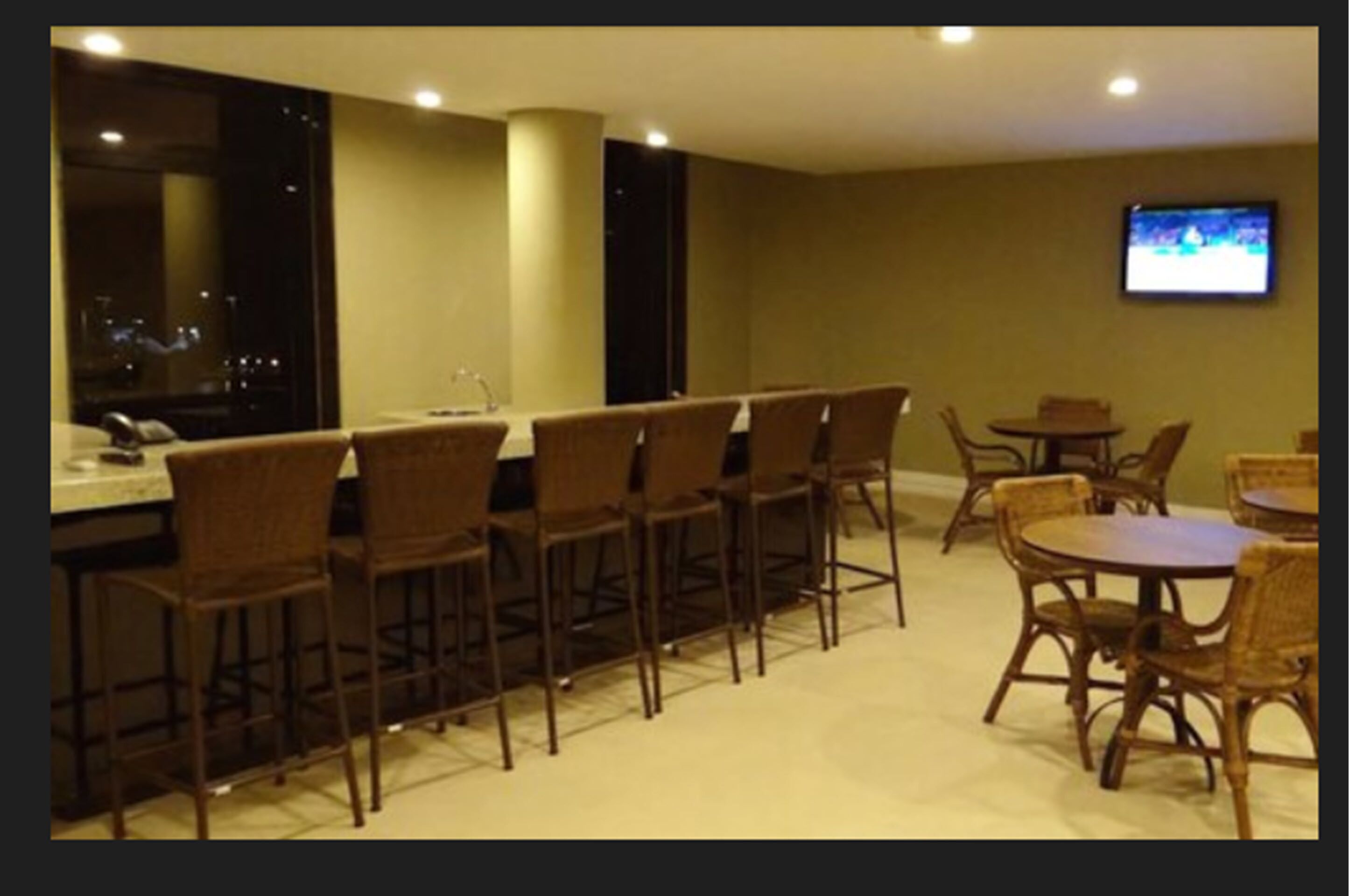 Habitación de hotel con área de bar, televisor montado en la pared y vista nocturna de la ciudad.