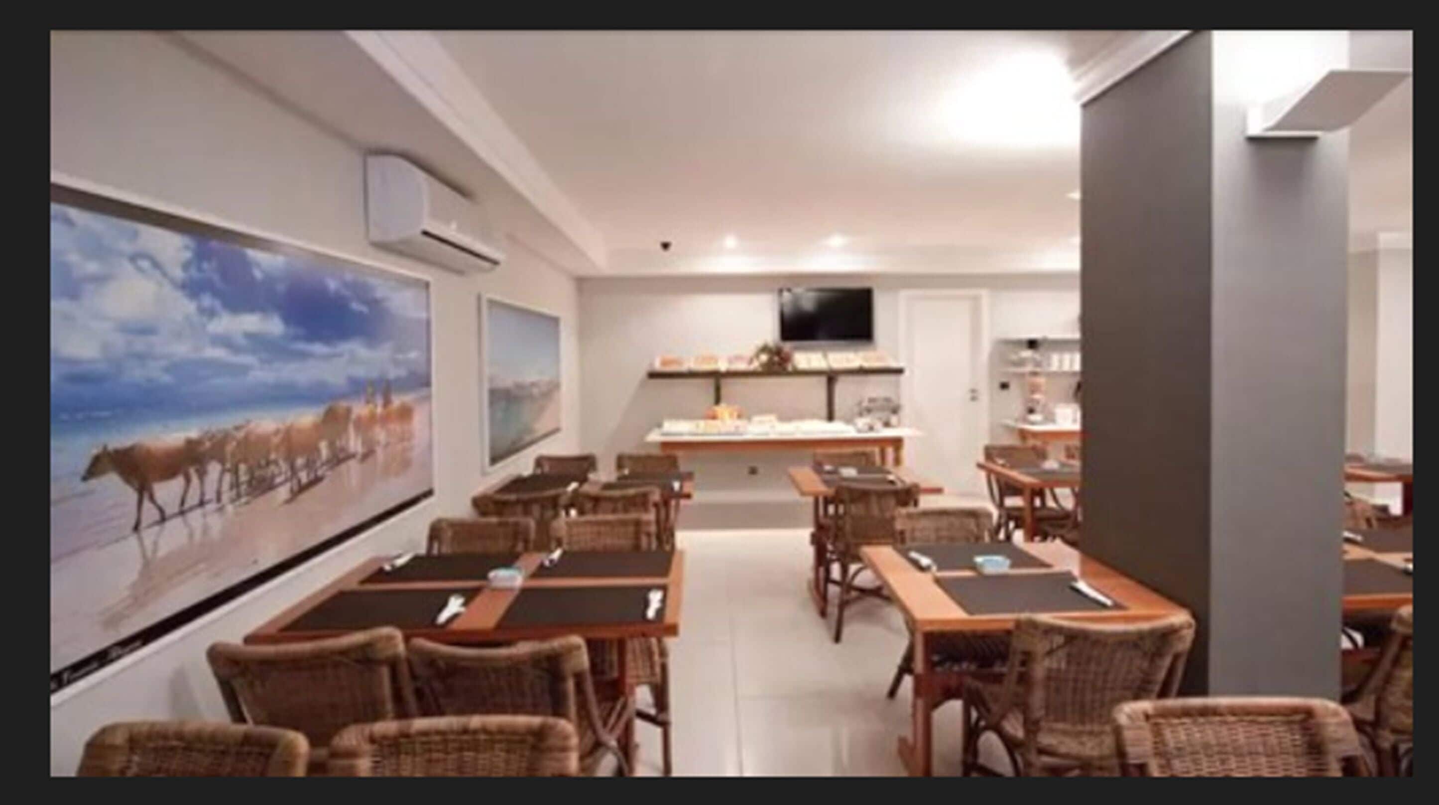 Un comedor con sillas y mesas de mimbre, un cuadro grande en la pared y un televisor de pantalla plana montado en la pared.