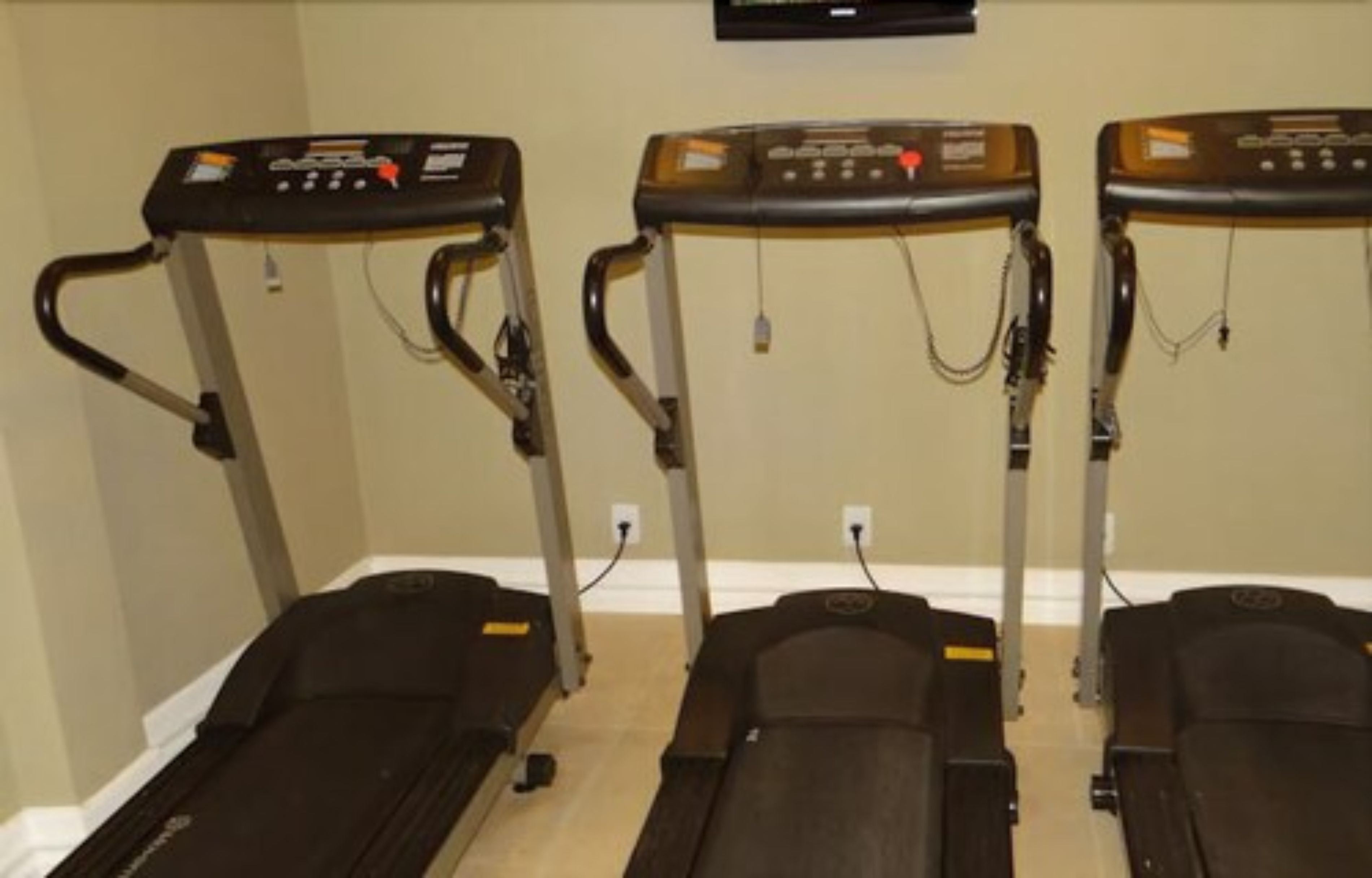 Three stationary bikes in a room with beige walls and a wooden floor.