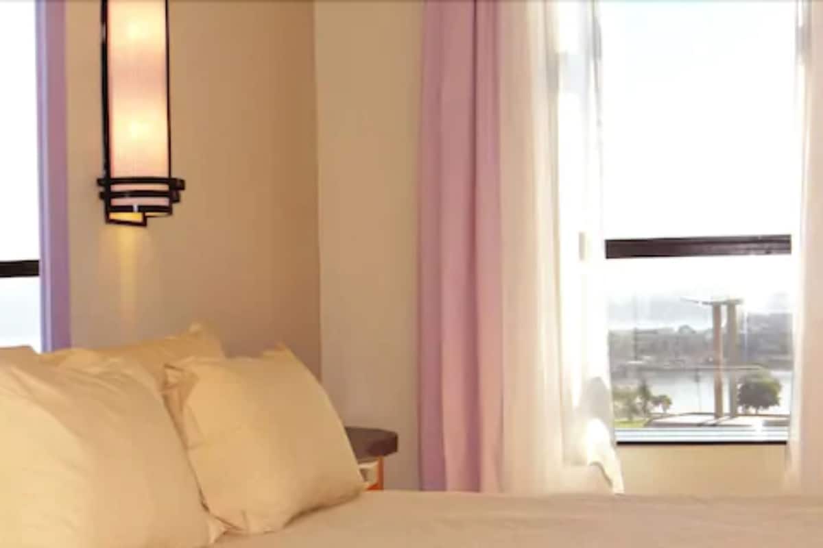 A hotel room with a bed, a nightstand, a lamp, and a window with curtains.
