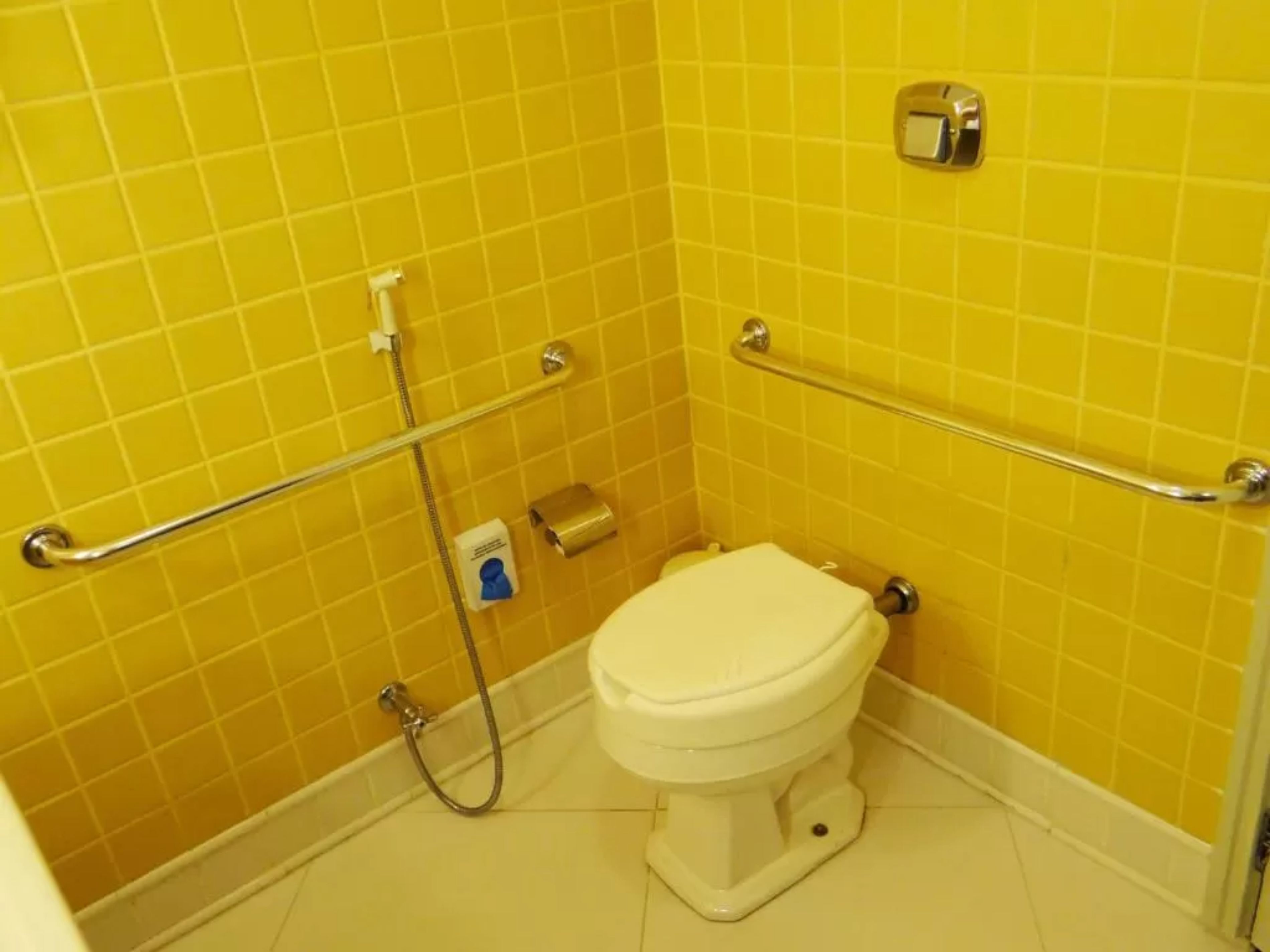 A small bathroom with yellow tiles, a white toilet, and a grab bar.