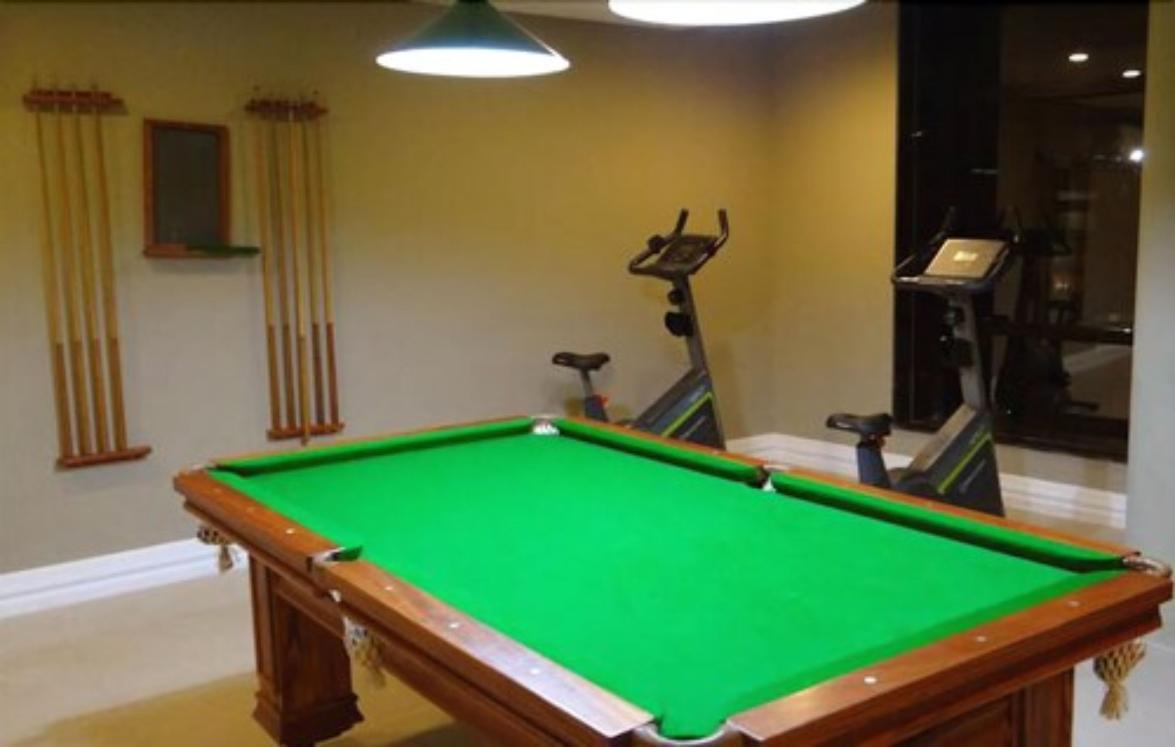 A pool table in a room with a treadmill and a small window.