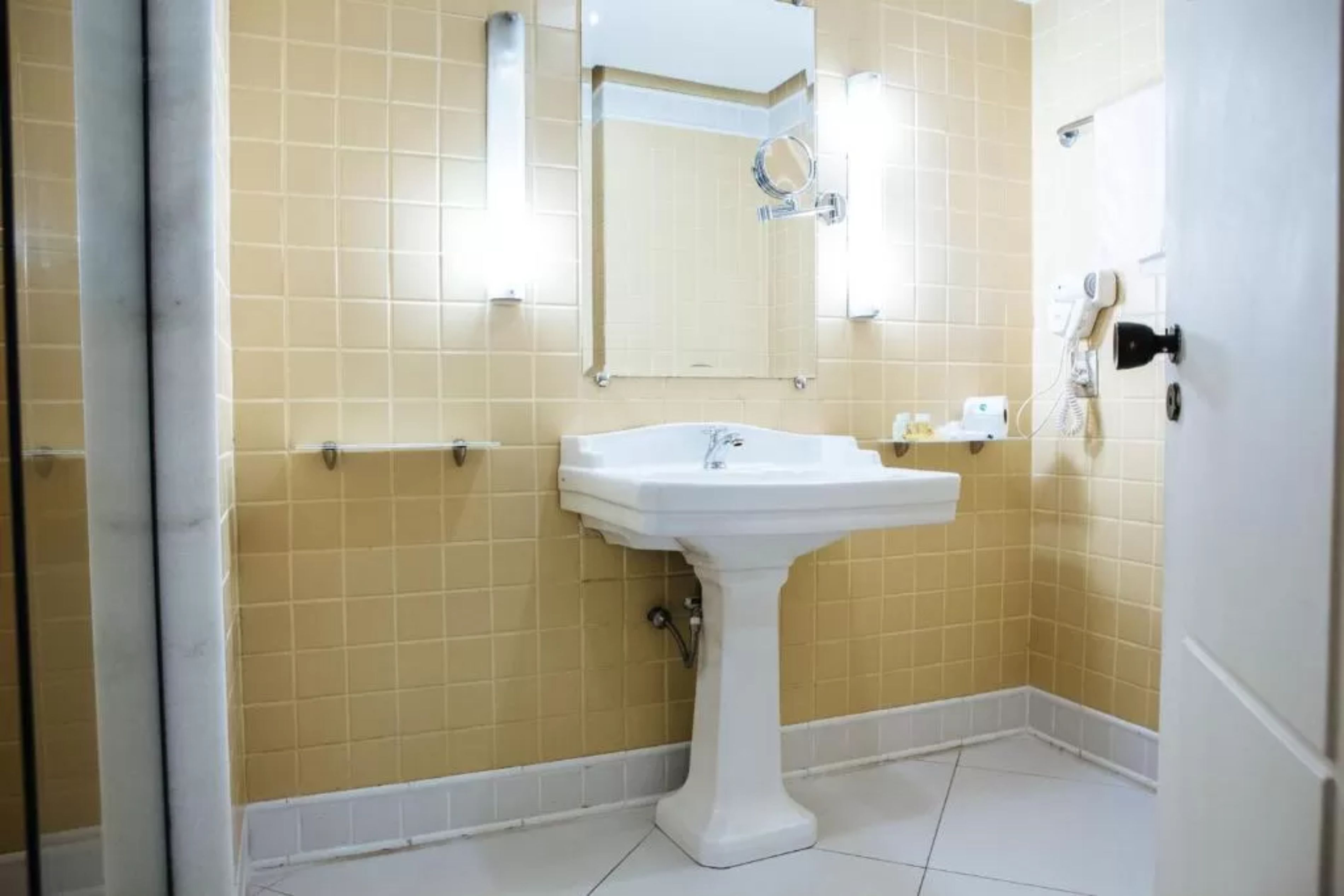 A bathroom with a pedestal sink, a mirror, and a towel rack.