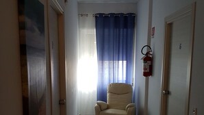 Un pasillo con un sillón color beige, un extintor y una puerta con el número 6.