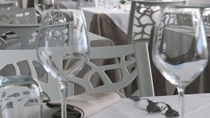 Un interior de restaurante con mesas dispuestas para comer, sillas y copas de vino.