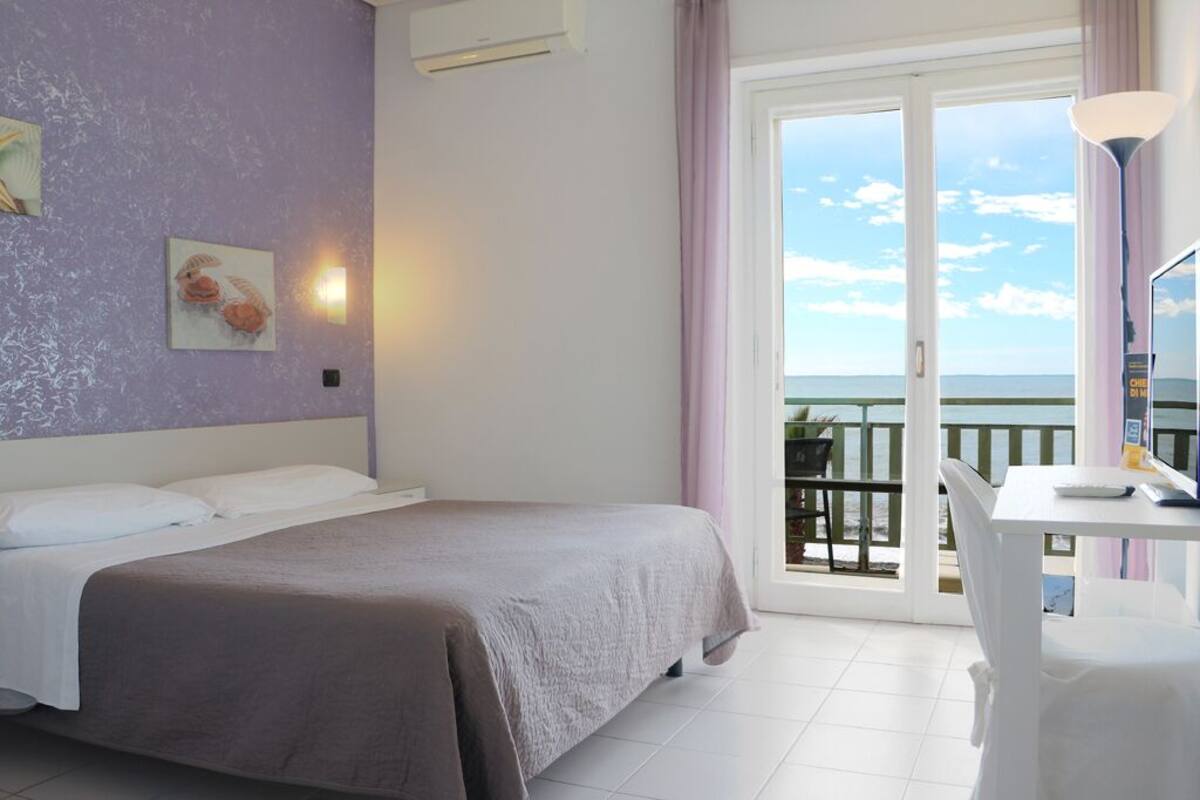 A bedroom with a bed, a desk, and a balcony with a view.