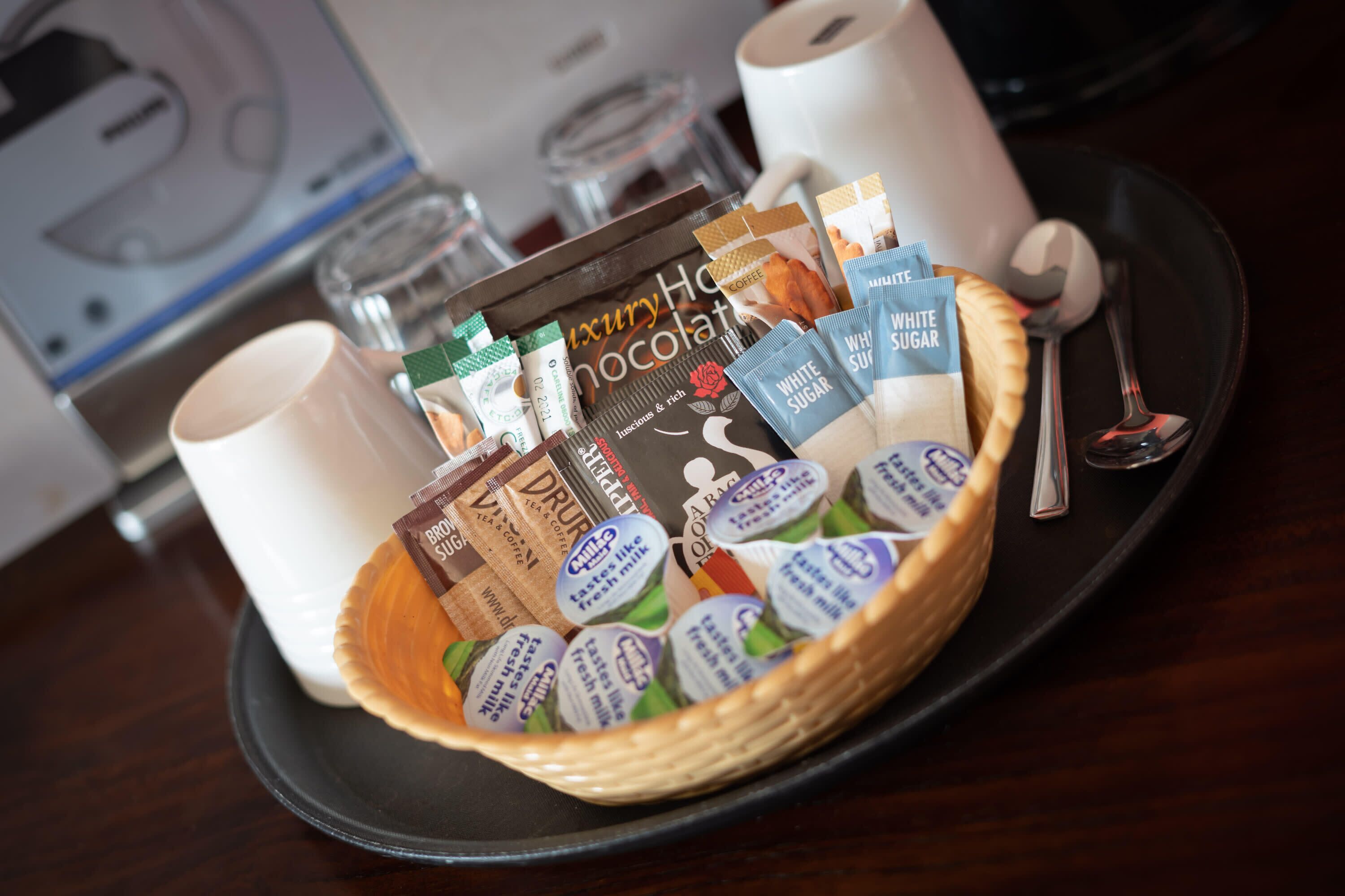 Un plateau avec un panier contenant des sachets de café et de thé, une cuillère et une tasse.