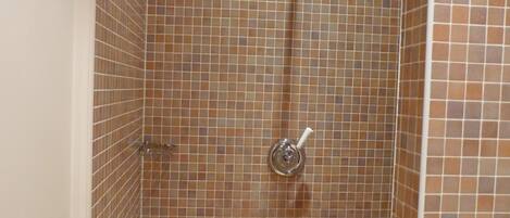 A shower with a handheld showerhead and a wall-mounted faucet.