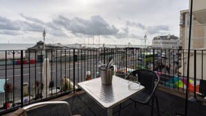 A balcony with a table and chairs overlooking a street and a body of water.