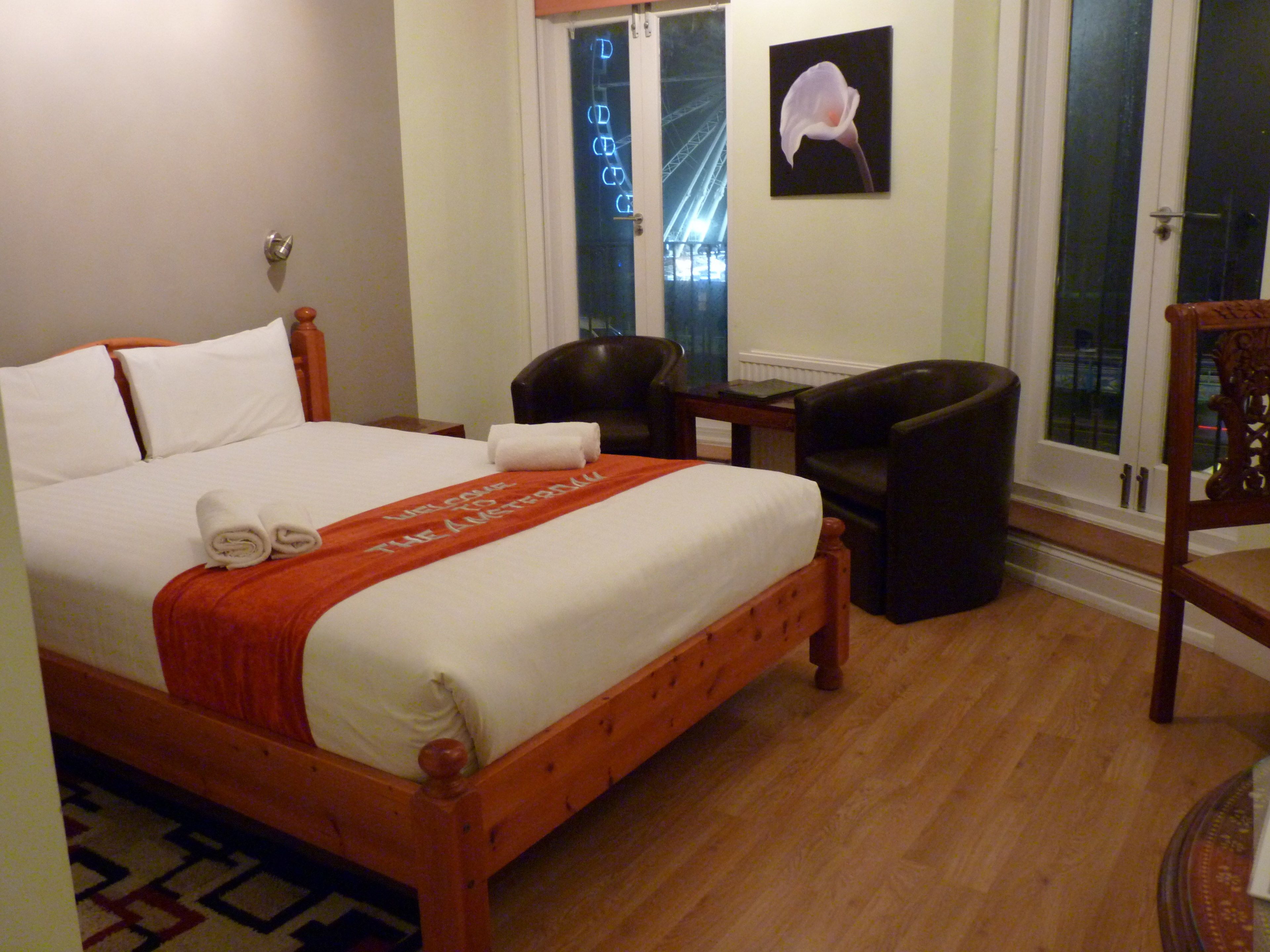 Une chambre d’hôtel avec un lit en bois, une chaise, un bureau et une fenêtre donnant sur un pont.