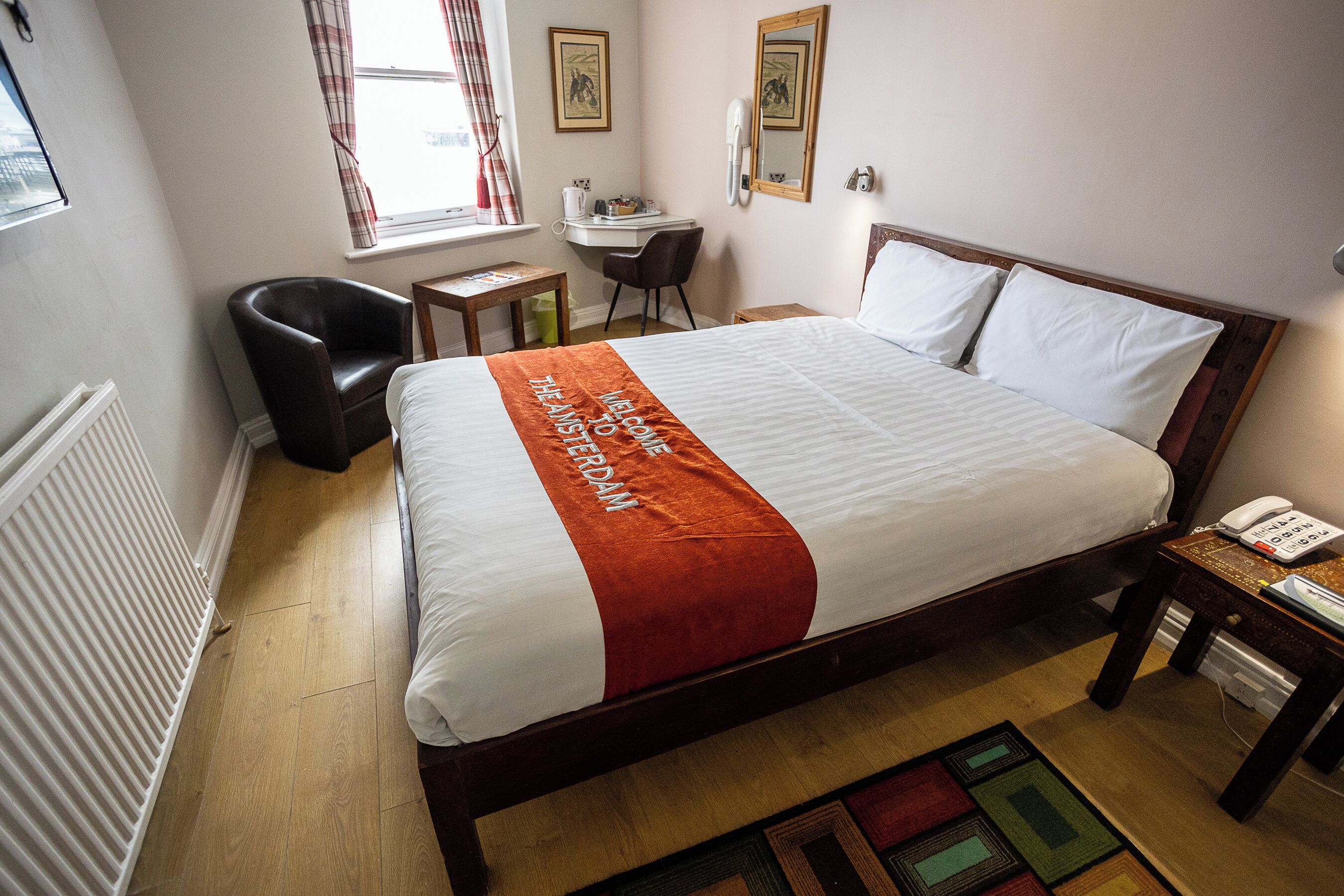 Habitación de hotel con una cama grande, un escritorio, una silla, un teléfono y un radiador.
