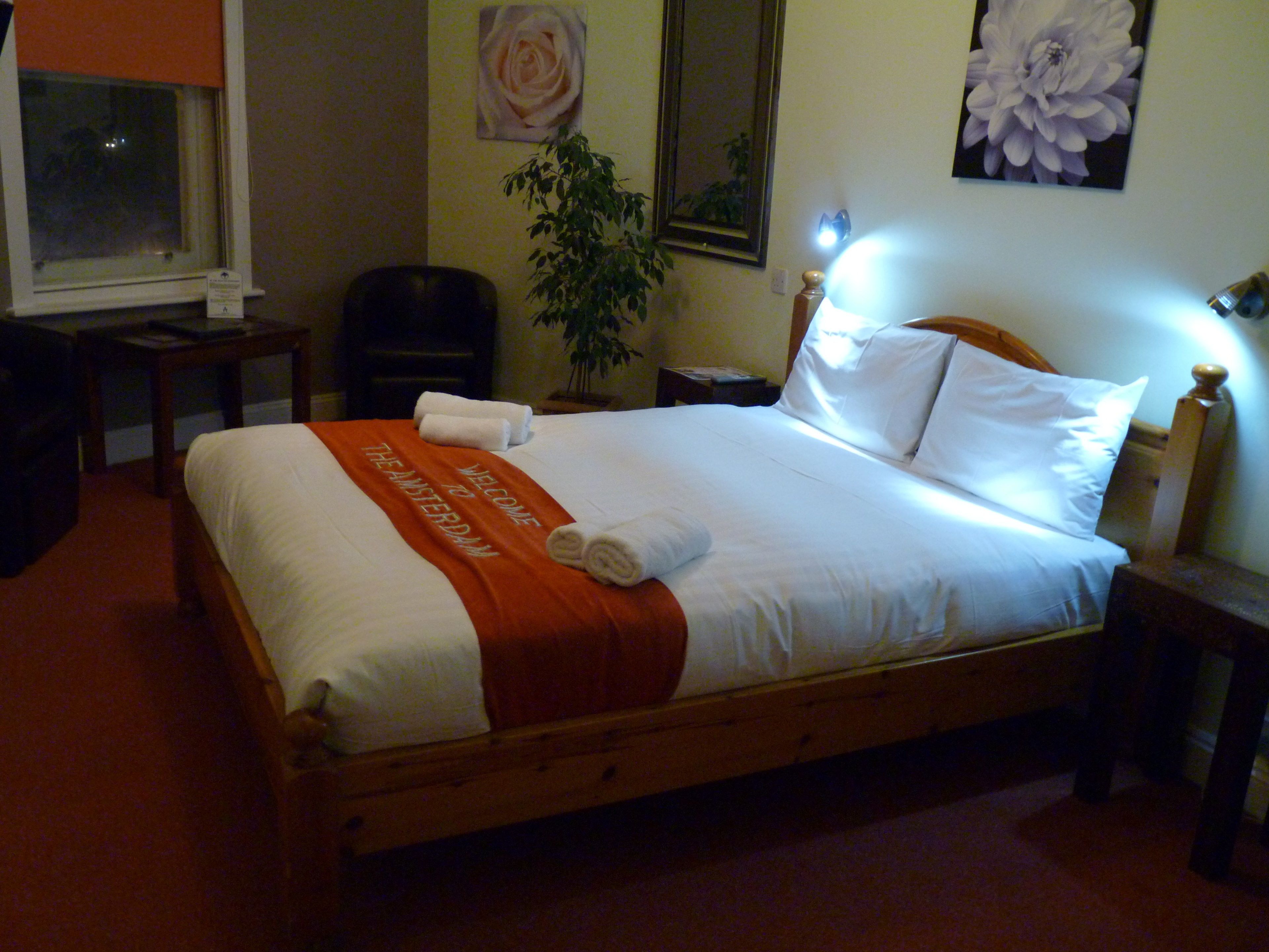 En pænt redt seng med et hvidt og orange sengetæppe, et træhovedgærde og et natbord med en lampe.