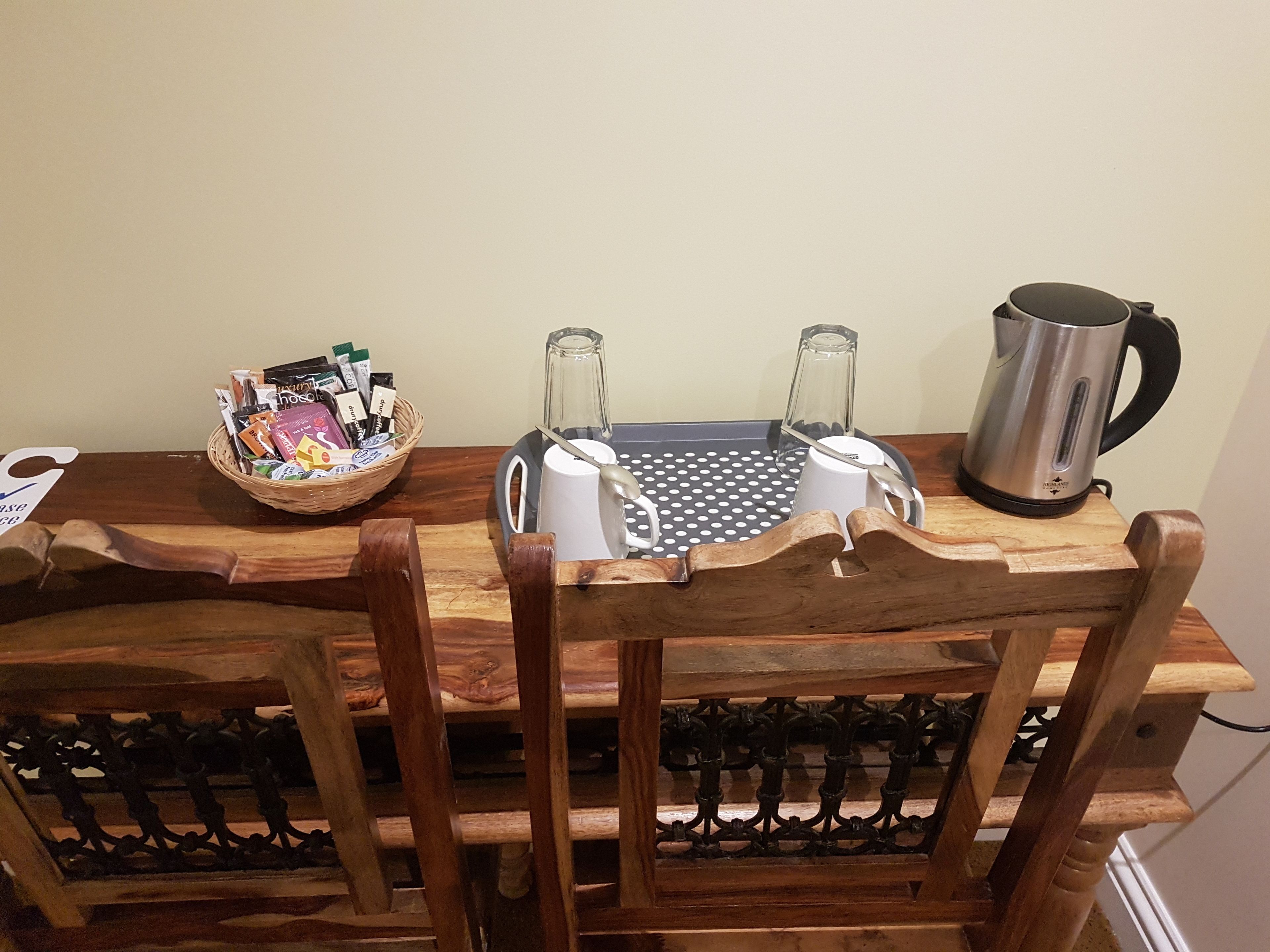 A wooden dining table with a basket of snacks, a blender, a kettle, and a coffee maker.