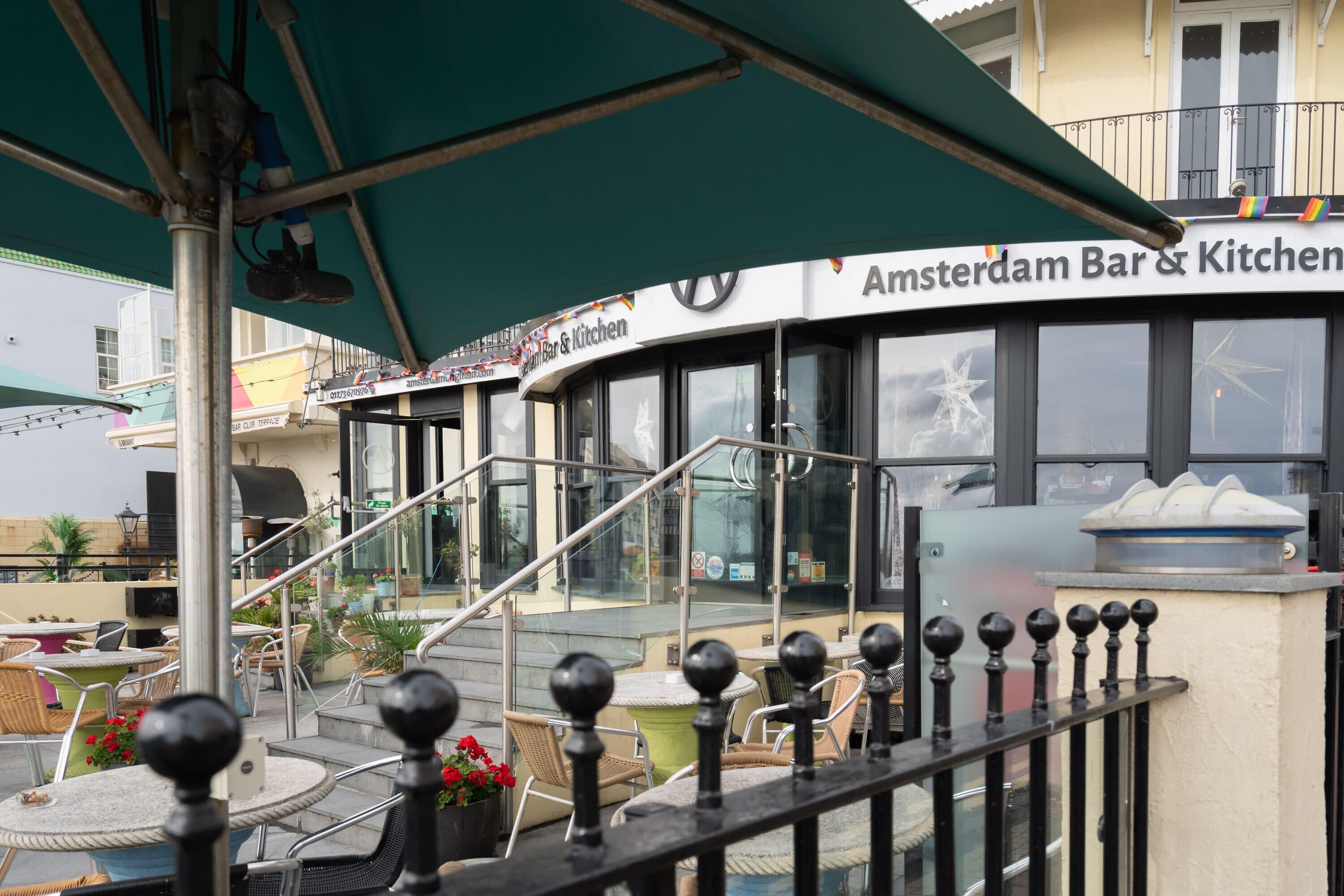 Un restaurante con terraza, un letrero que dice 'Amsterdam Bar & Kitchen' y una escalera que conduce a un nivel superior.