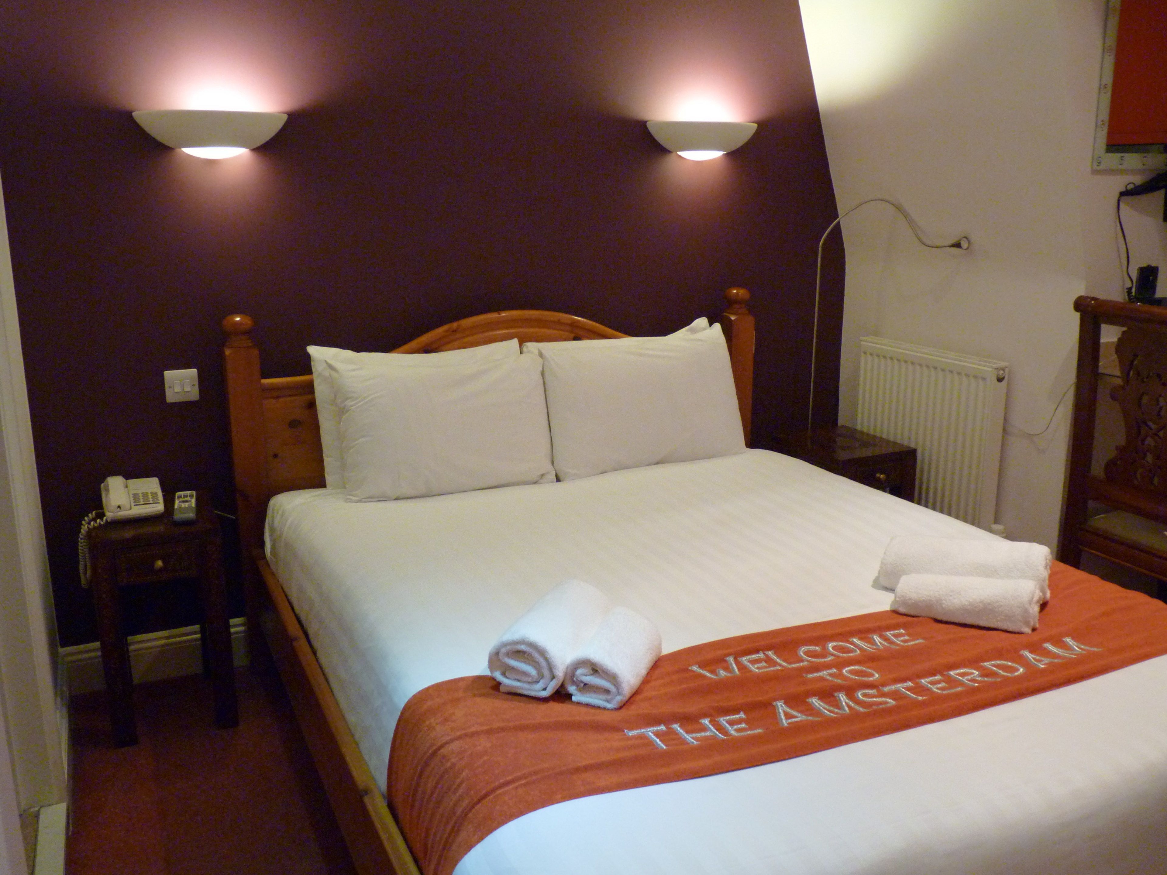 A hotel room with a bed, a nightstand with a telephone, and a wall-mounted light fixture.