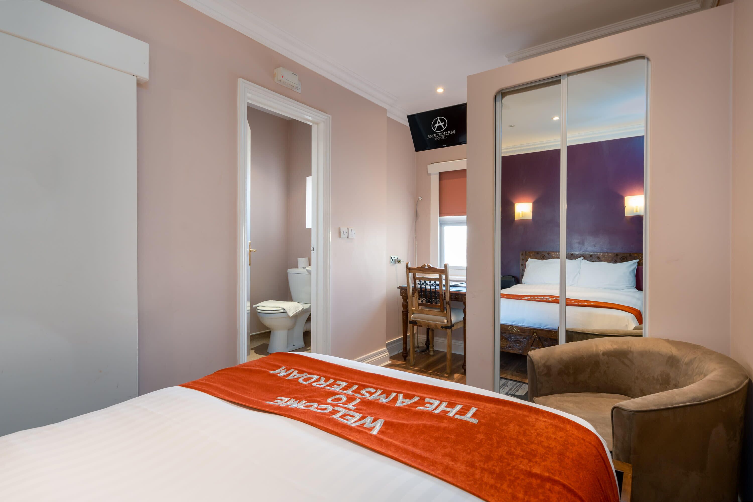Quarto de hotel com cama, cadeira, mesa de trabalho e banheiro.