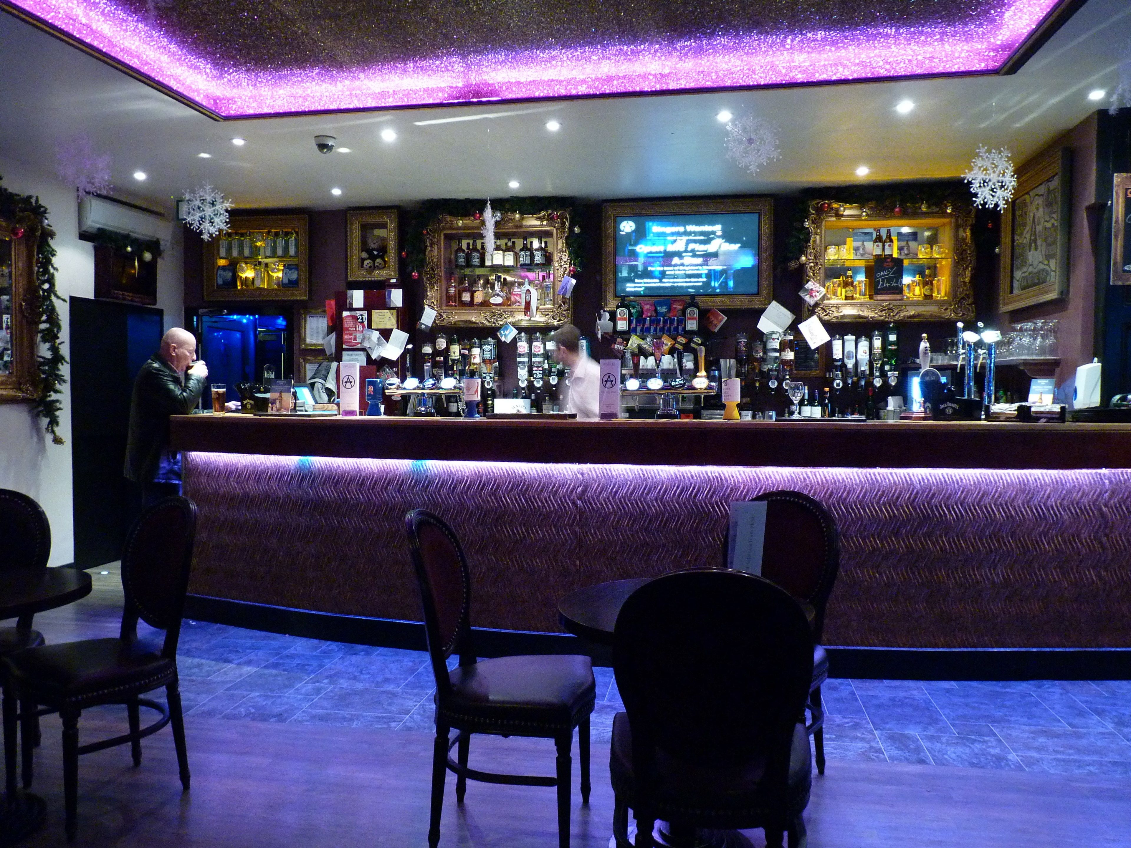 Un área de bar con mostrador, sillas y una pantalla mostrando un menú.