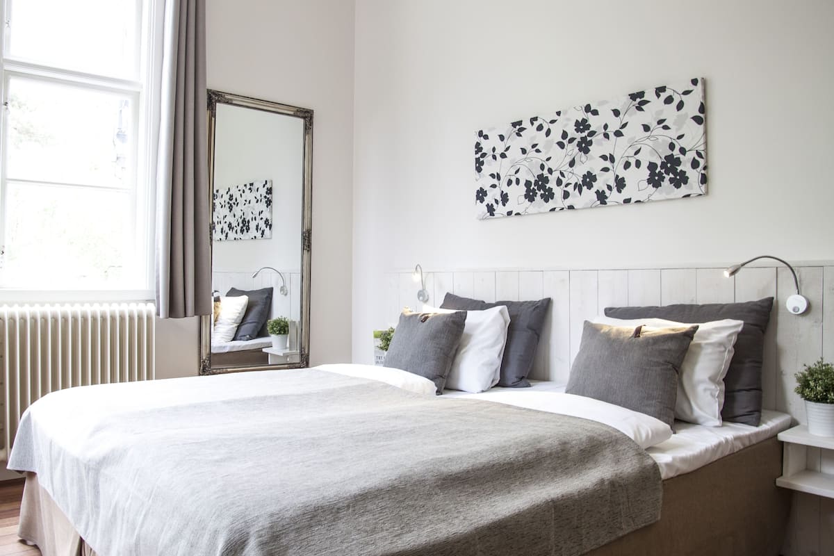 A bedroom with a large bed, a nightstand, a mirror, and artwork on the wall.