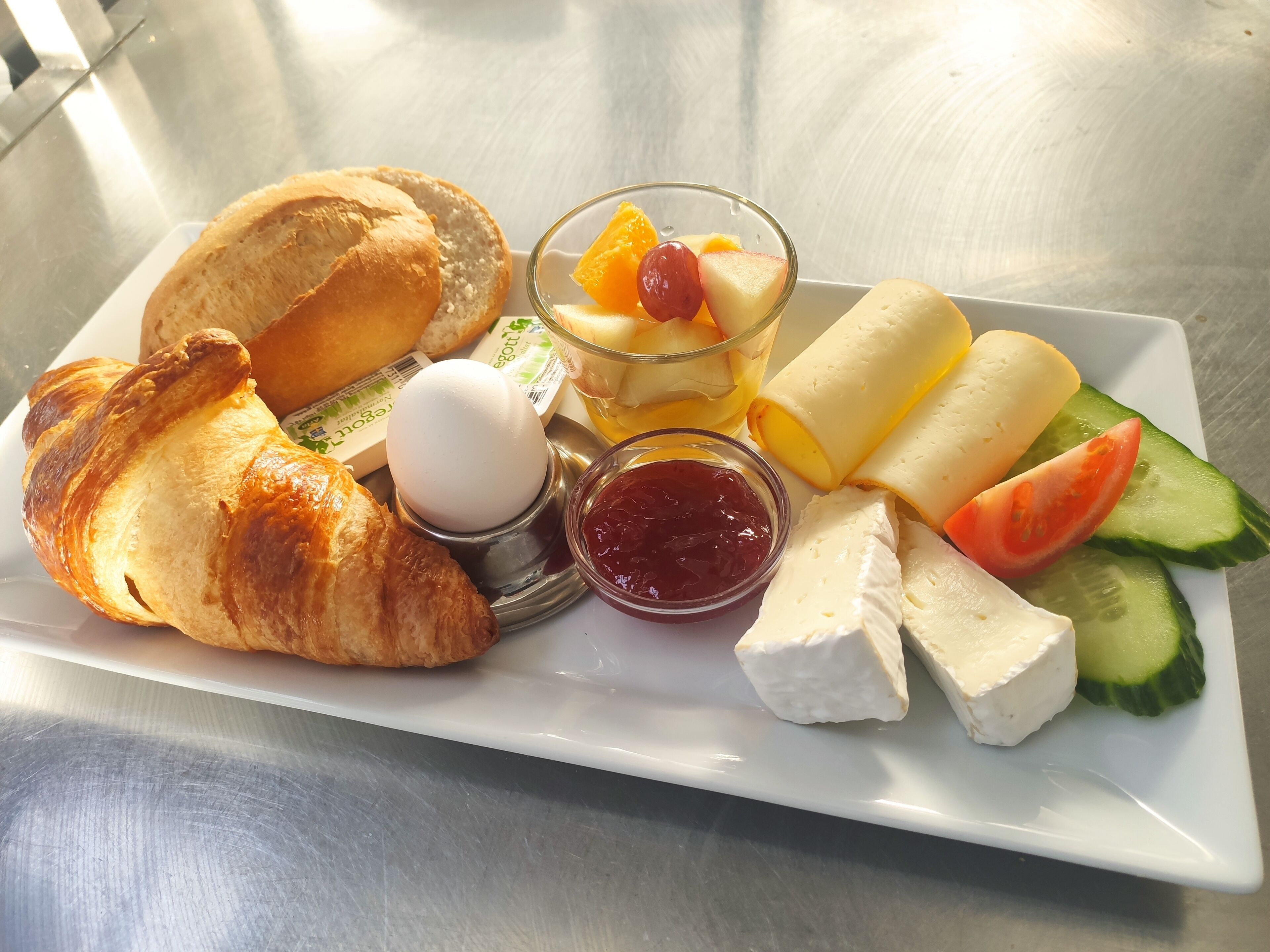 A breakfast plate with croissants, cheese, fruit, and jam.