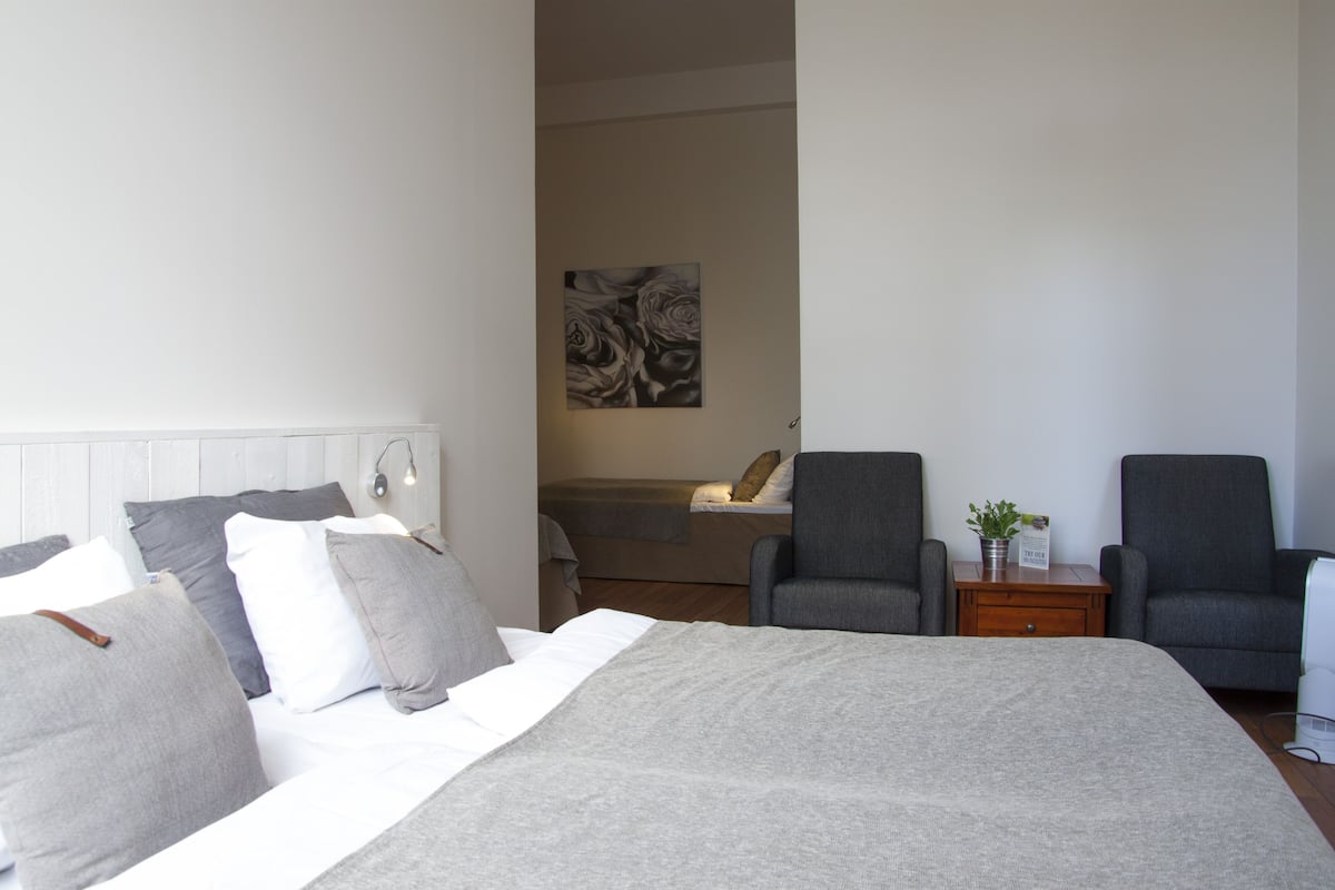 A hotel room with a large bed, two armchairs, a small table with a plant, and a painting on the wall.