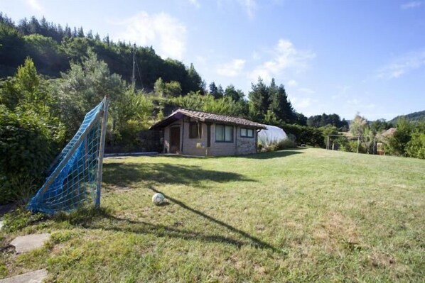A small house with a tiled roof, surrounded by a grassy yard and trees.