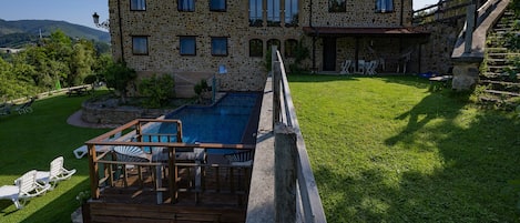 A stone building with a swimming pool, deck chairs, and a stone staircase.