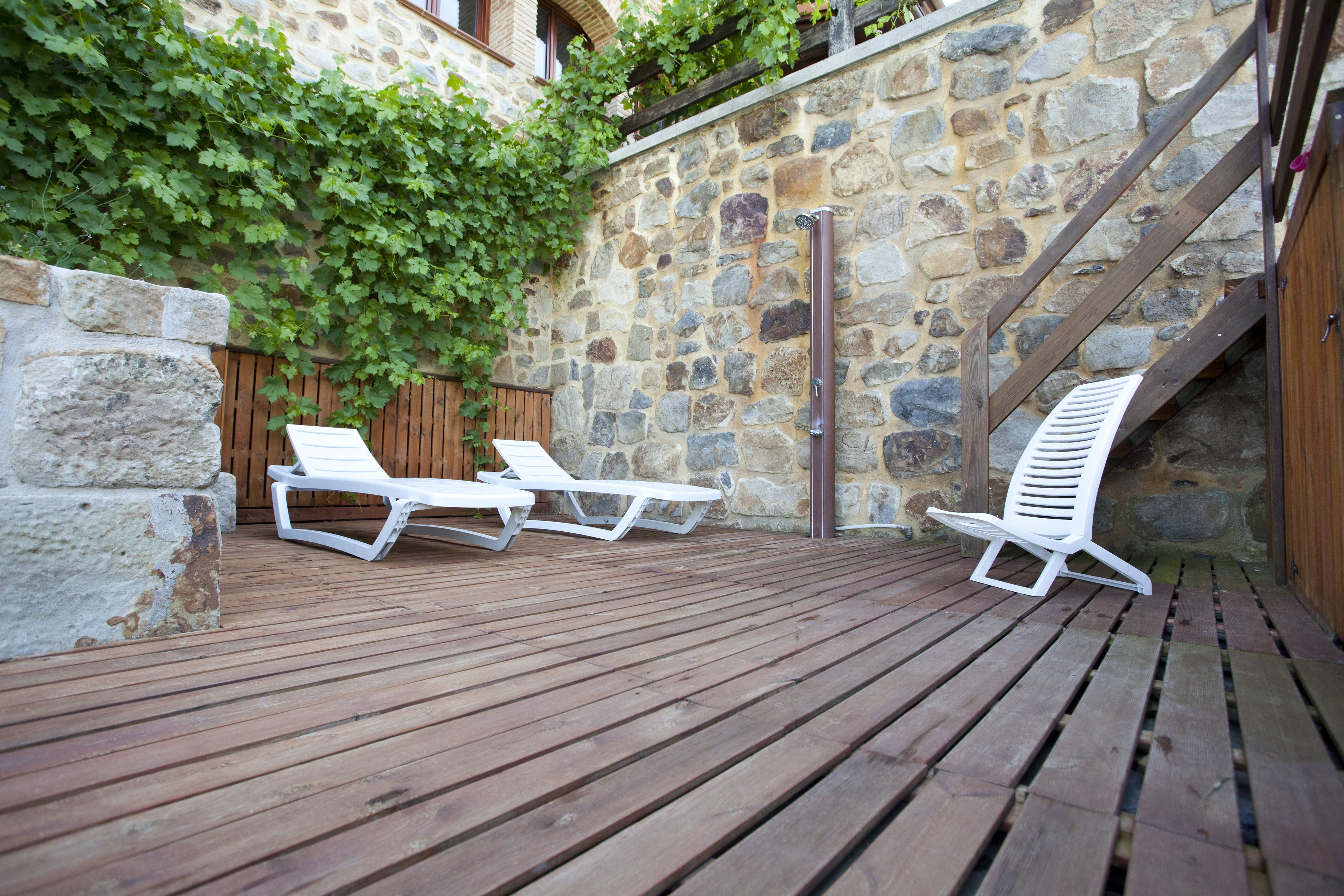 A wooden deck with lounge chairs, a stone wall, and a wooden staircase.