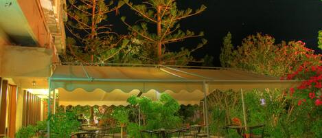 Un espace extérieur aménagé en terrasse, avec des tables et des chaises, entouré de plantes en pot et d’arbres.