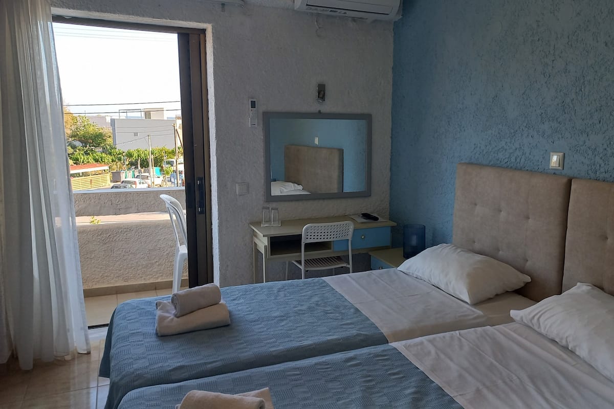 A hotel room with two beds, a desk, a chair, a mirror, and a view of the outside.