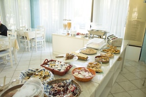 A buffet setup with various food items and a seating area with white chairs and tables. - Hotel Esperides (Ierapetra)