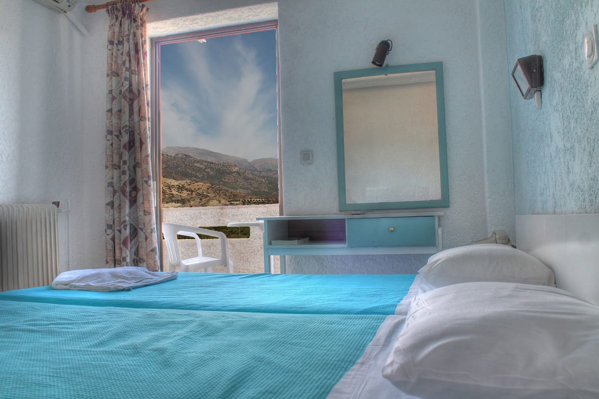 A bedroom with a bed, a desk, and a view of the outdoors.