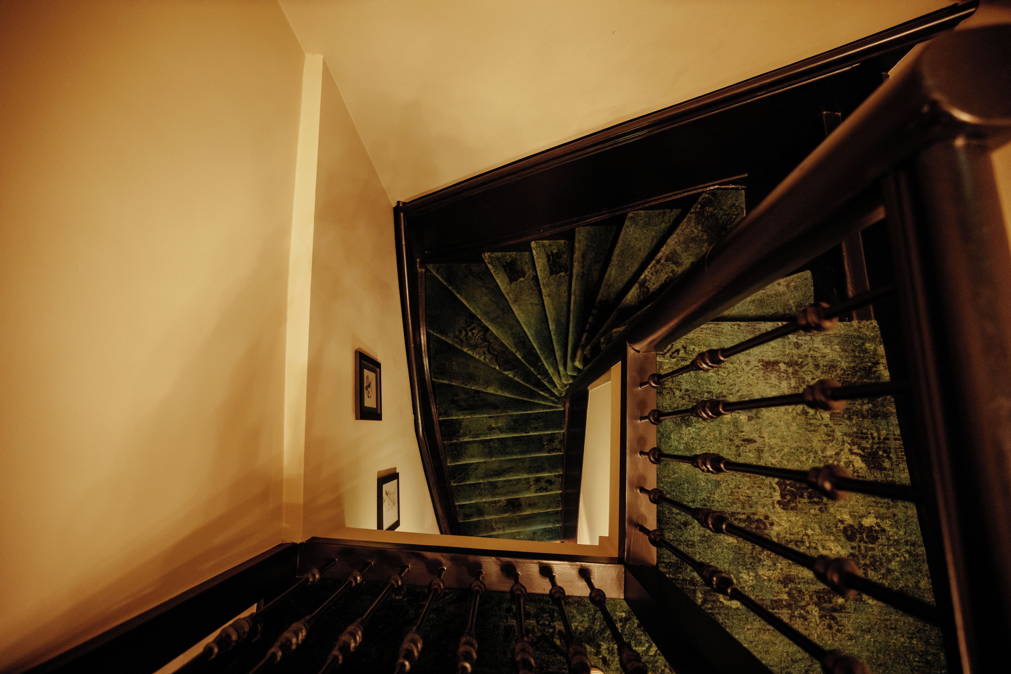 A spiral staircase with a wooden handrail and a green, moss-covered wall.