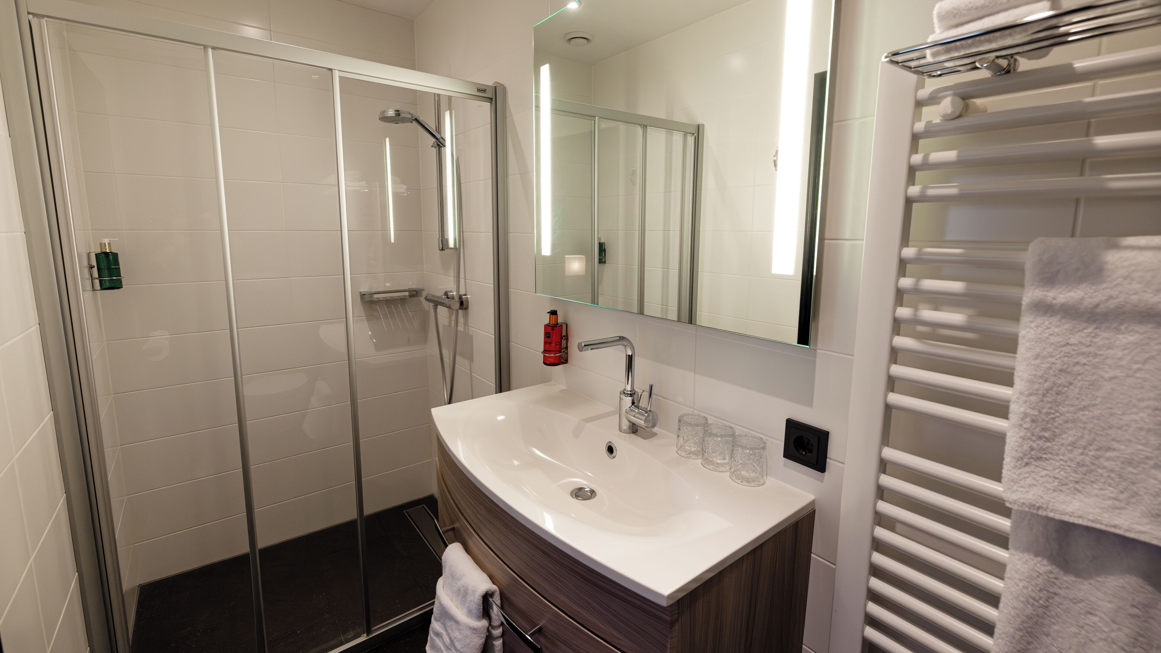 Een moderne badkamer met een glazen douchecabine, een wit wastafelmeubel en een handdoekhouder.