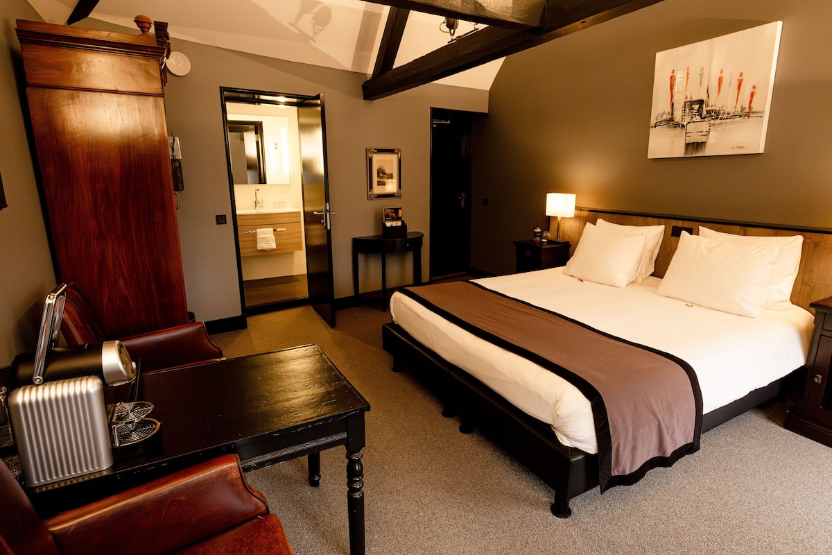Une chambre d’hôtel avec un grand lit, un bureau, une chaise, une table de chevet et un tableau au mur.