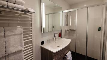 A modern bathroom with a white sink, mirror, and glass-enclosed shower.